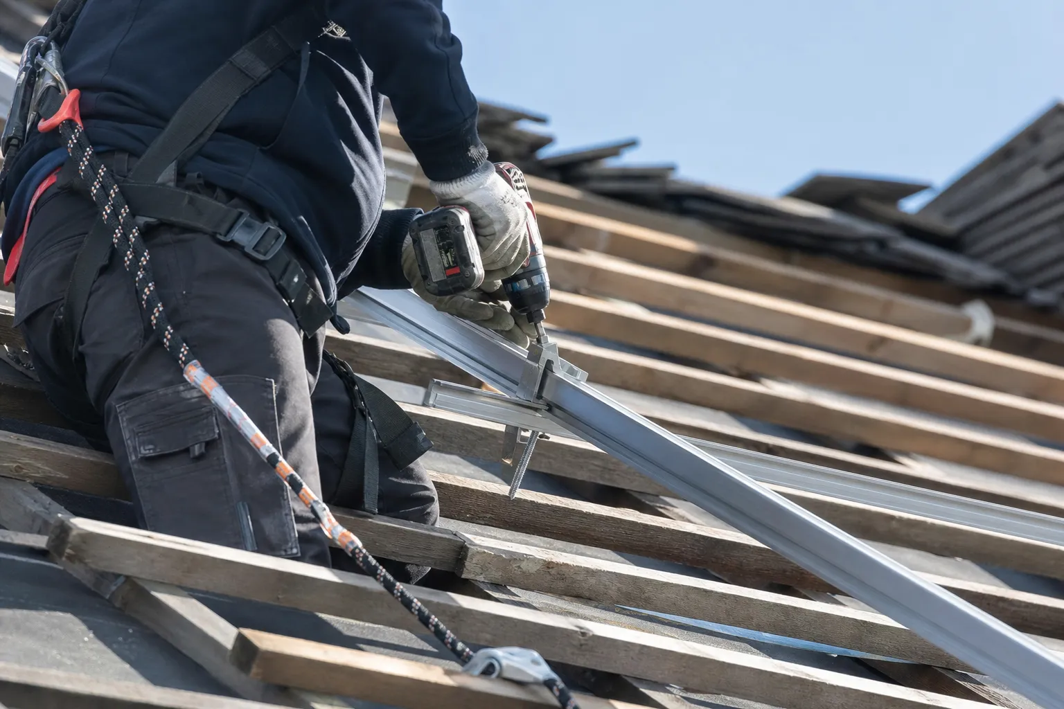 Installateur en harnais de sécurité fixant un rail de panneau solaire sur une toiture en pente