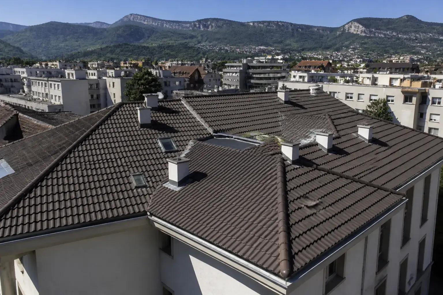 Toiture d’immeuble collectif de faible hauteur en quartier urbain, contreforts montagneux au loin