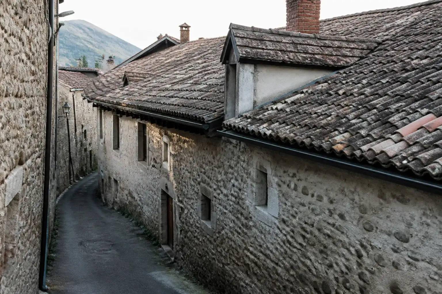 Toiture ancienne en tuiles patinées d’une maison de centre-bourg, ruelle de village de piémont alpin
